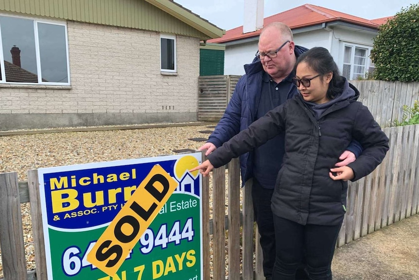 A man and a woman point at a sold sign on a fence.