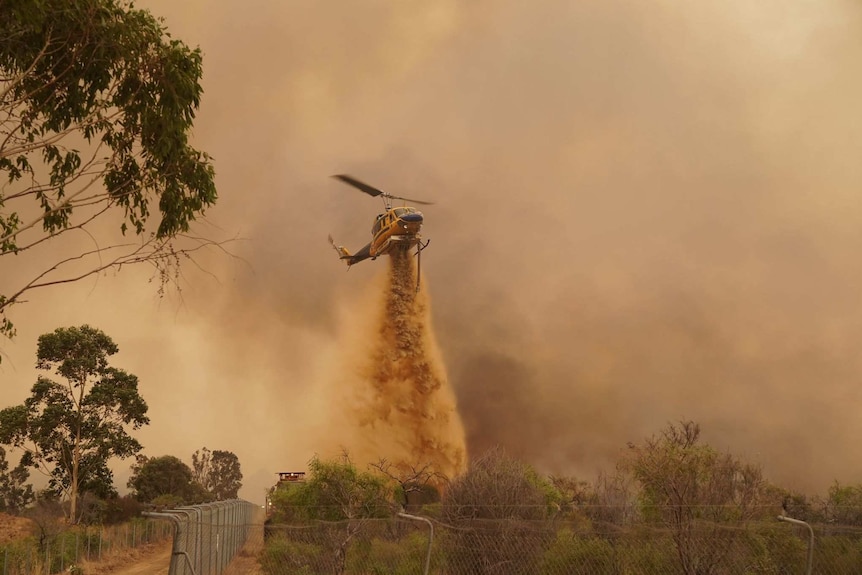 A helicopter drops water against a smoke darkened sky.