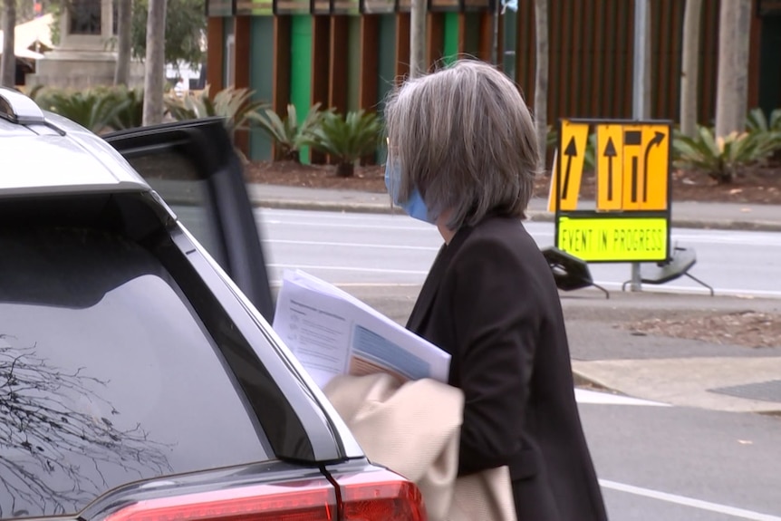 A woman getting into a car holding a coat and papers