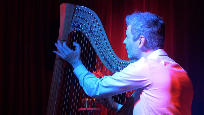Man playing harp with red and  blue lighting.