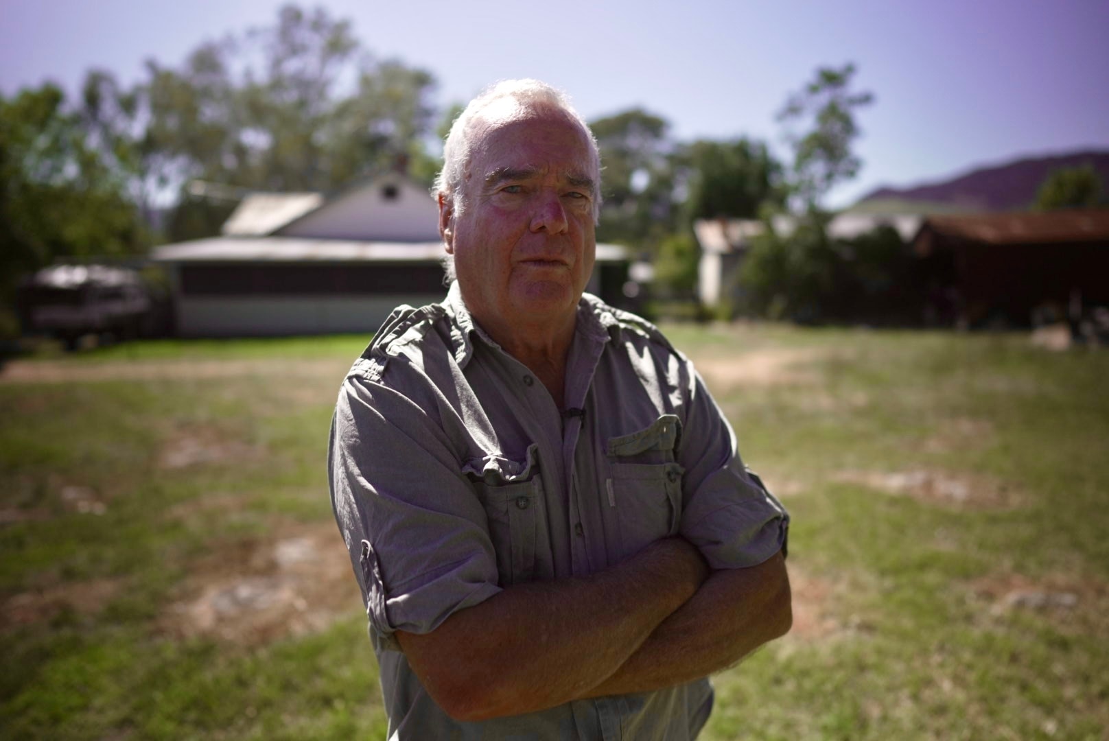 Man with his arms crossed standing on a grassy field.