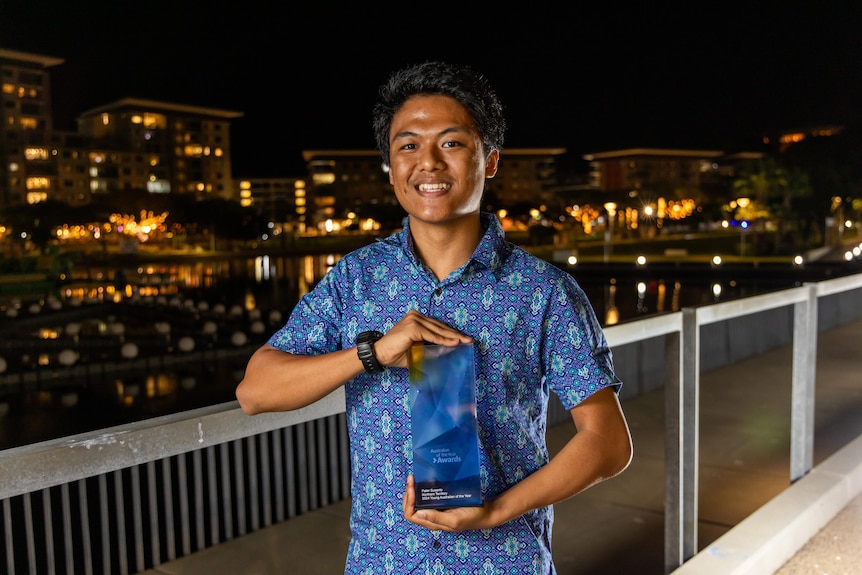 A young man in a button up shirt holds a glass award.