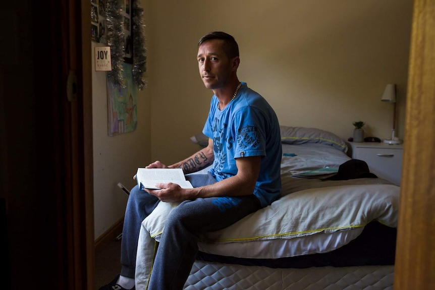 Ashley Hobbins sits on a bed and holds open a book.