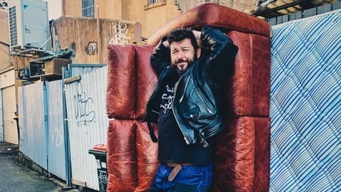 a man poses with a red couch he found on a street