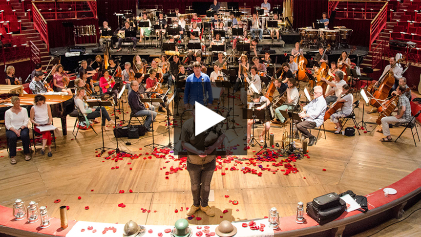 A photo of an orchestra in rehearsal. A bagpipe player is performing in the foreground.