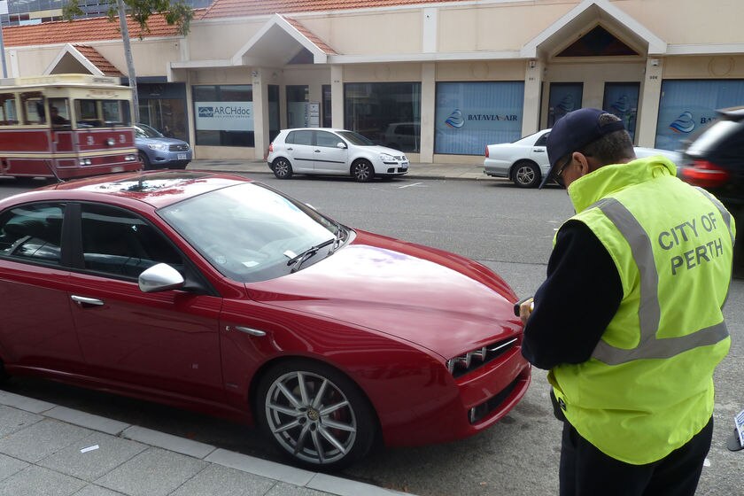 City of Perth parking inspector handing out ticket to red car on street as tram goes by