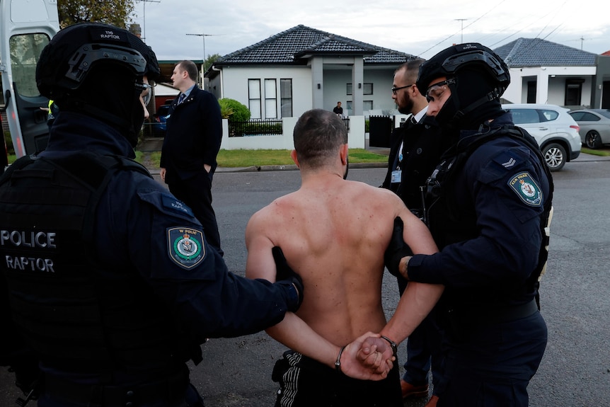 A shirtless man being led onto the road by police