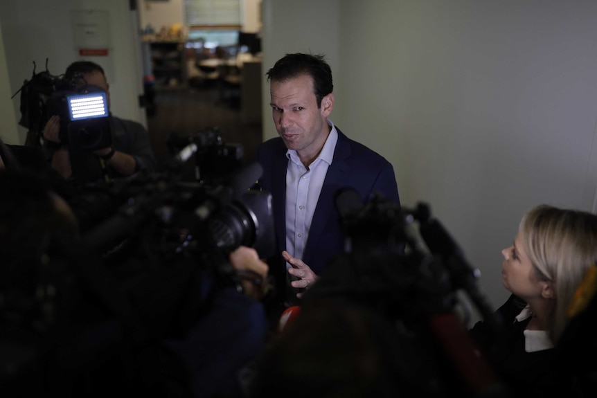 Matt Canavan stands in a corridor surrounded by cameras and journalists