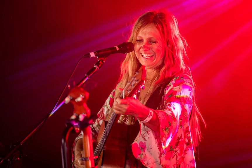 Musician Kasey Chambers holds a guitar and sings in front of a microphone