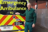 Paramedic in green work clothes with grey hair stands next to ambulance