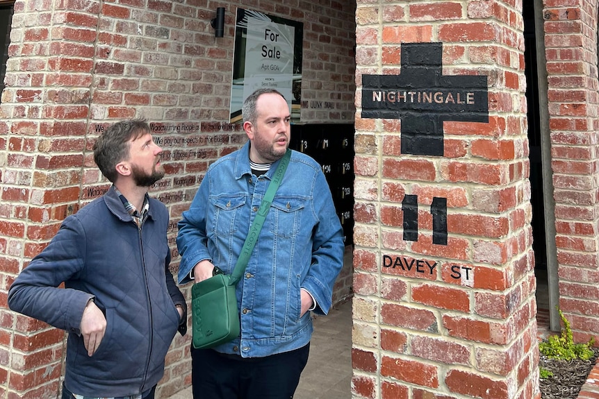 two men stand in front of a red brick building