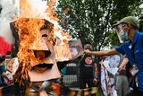 A two-headed effigy depicting Rodrigo Duterte and Ferdinand Marcos Jr is burned in the streets by protesters holding photos.