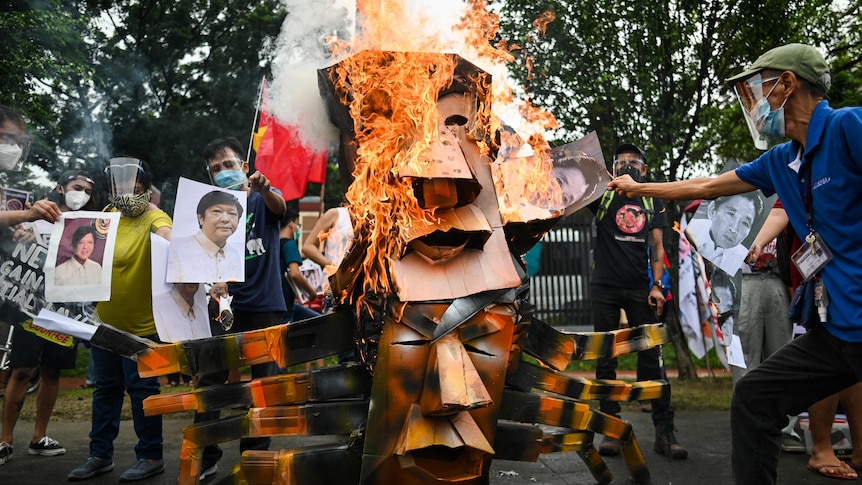 A two-headed effigy depicting Rodrigo Duterte and Ferdinand Marcos Jr is burned in the streets by protesters holding photos.