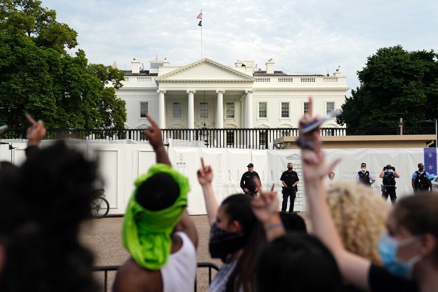 a crowd of protesters direct obscene gestures to the White House. Secret Servicemen stand around the perimeter fence