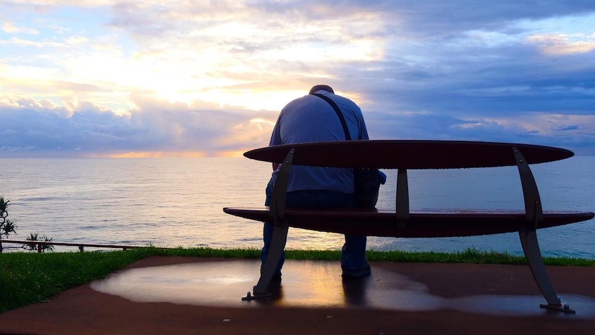 man sitting on bench in front of ocean