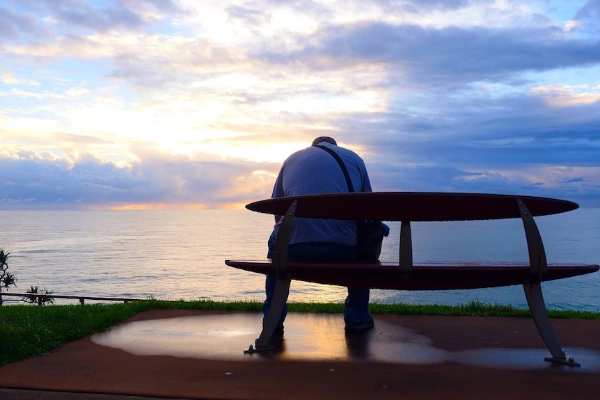 man sitting on bench in front of ocean