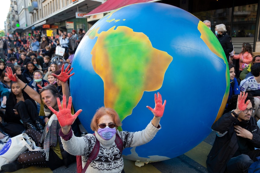 Protesters with red paint on their hands in front of a blow-up globe. 