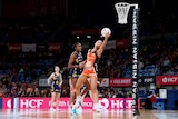 A Giants Super Netballer reaches out near the basket and catches the ball in the palm of her left hand as a defender trails. 