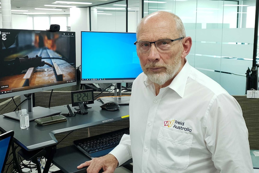 A man wearing a white shirt and glasses at a computer.