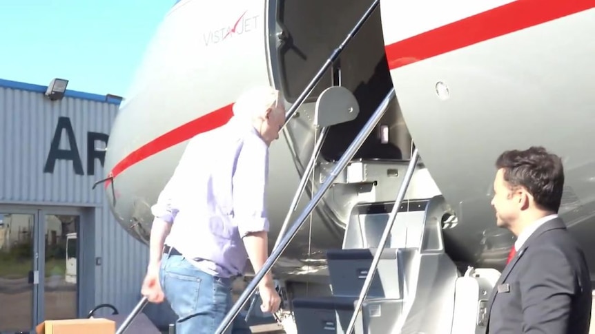 Julian Assange ascends stairs into an airplane.