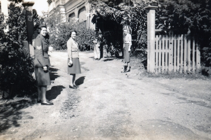 black and white photo shows three women in uniform looking backwards and they walk up a dirt driveway