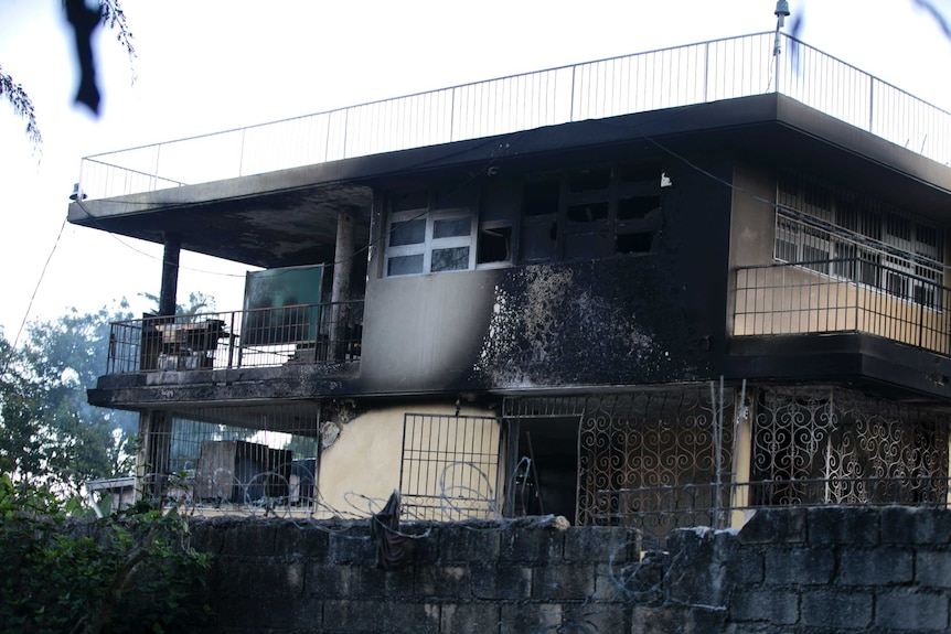 A burnt our building sits behind an also burned concrete wall topped with barbed wire in Haiti.