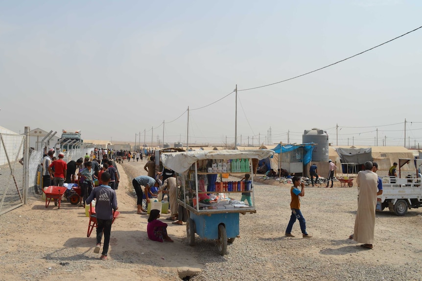 a food cart and group of people on a dirt track in the displaced person's camp in Iraq