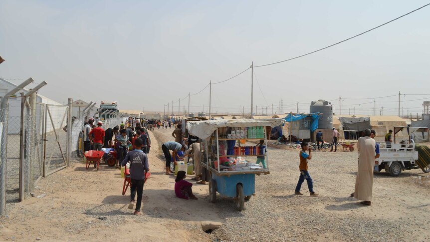 a food cart and group of people on a dirt track in the displaced person's camp in Iraq
