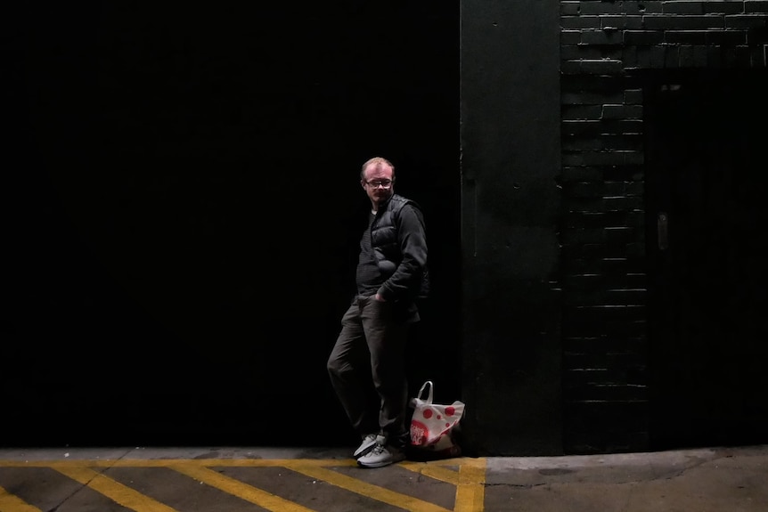 A man walks past a brick wall in the dark.