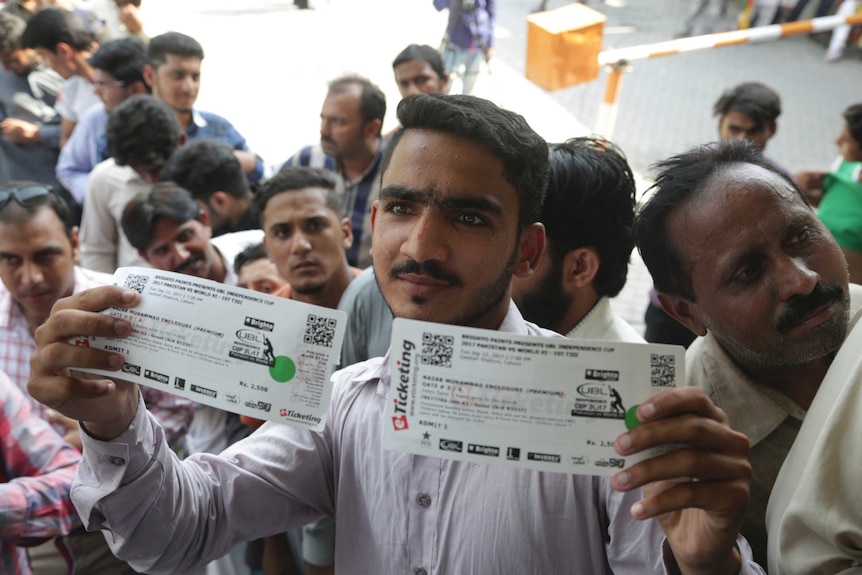 A man holds up two tickets while surrounded by people.