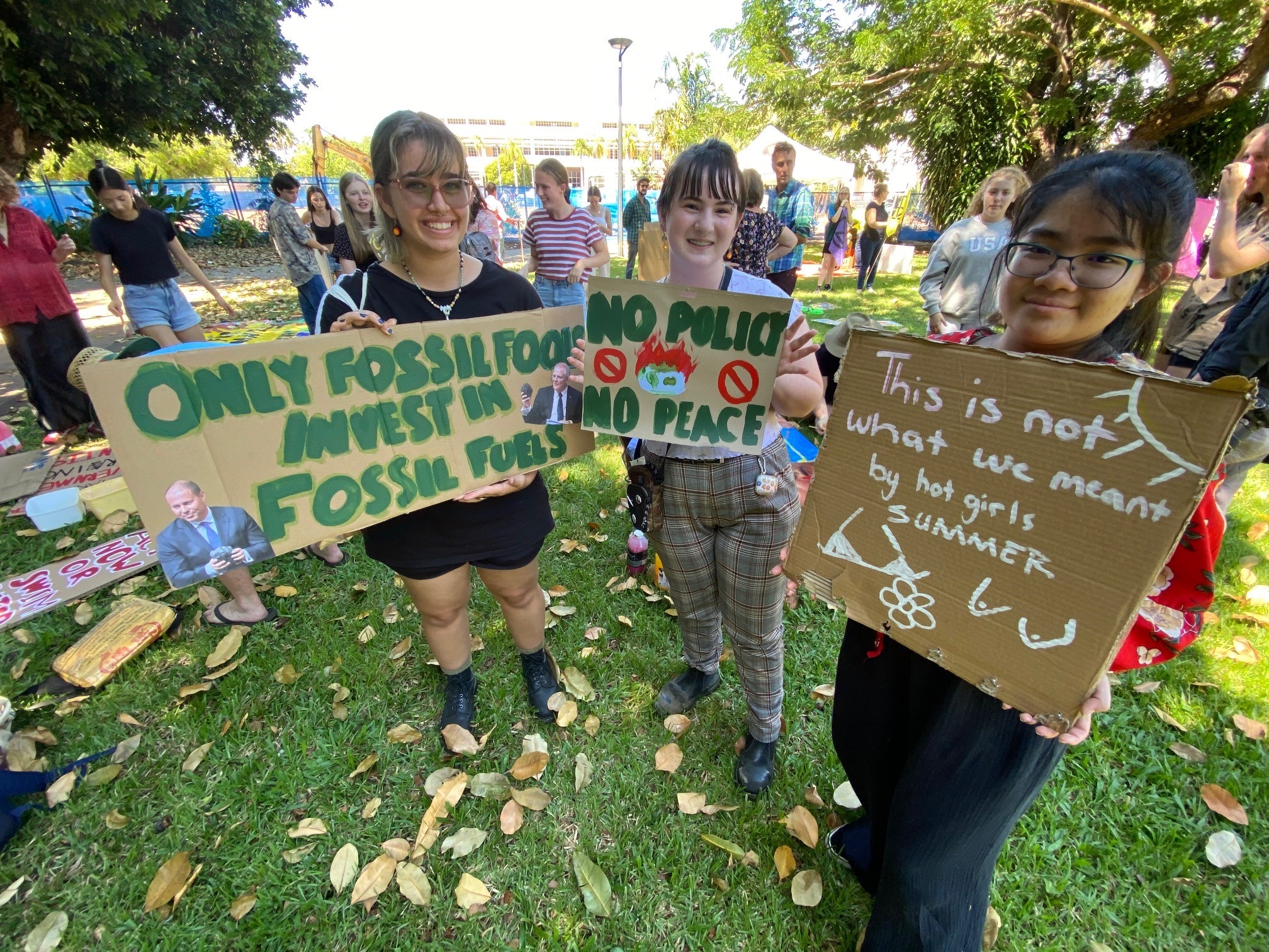 Three young people stand at a climate change protest holding witty signs and smiling.