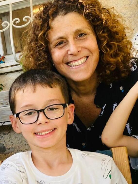 A woman with brown curly hair and a dark-haired boy wearing glasses smile at the camera