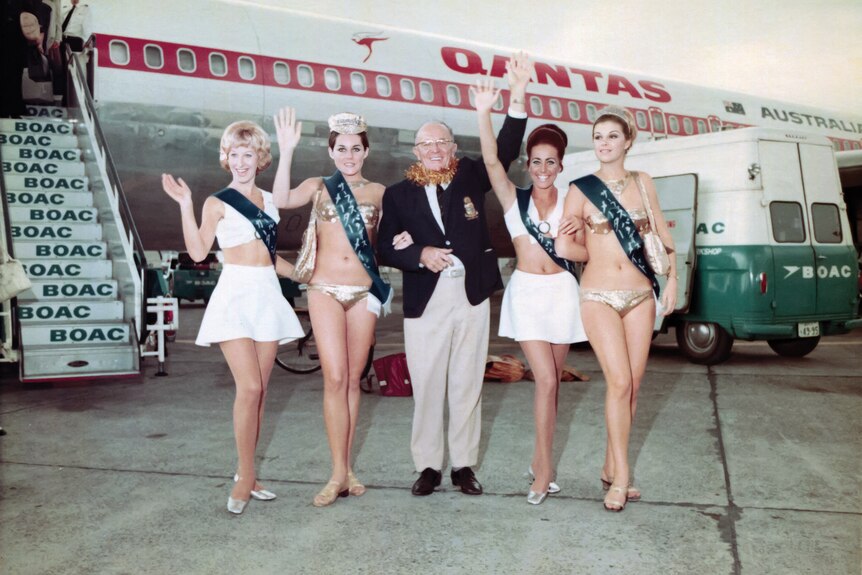 man standing in front of Qantas plane with four women in bikinis