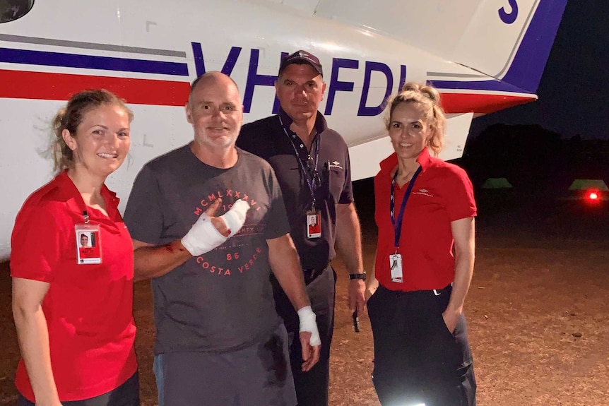 Survivor Craig Dickmann with a bandaged hand stands in front of a plane with staff from the Royal Flying Doctor Service.