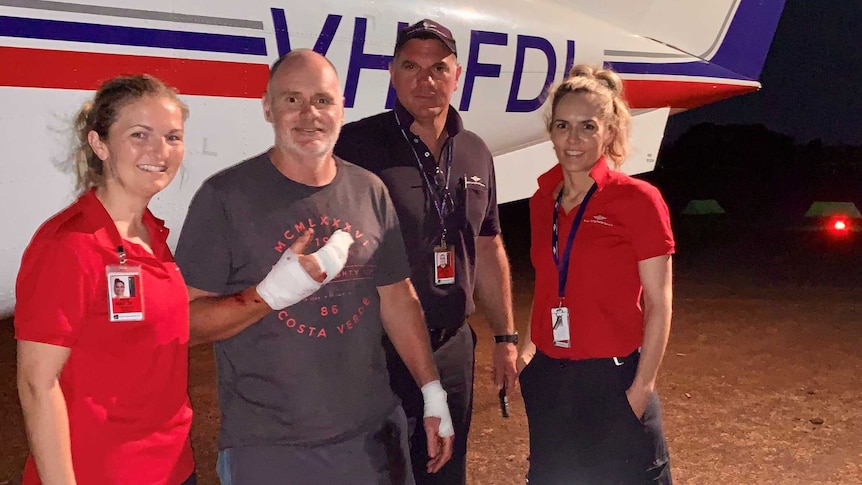 Survivor Craig Dickmann with a bandaged hand stands in front of a plane with staff from the Royal Flying Doctor Service.