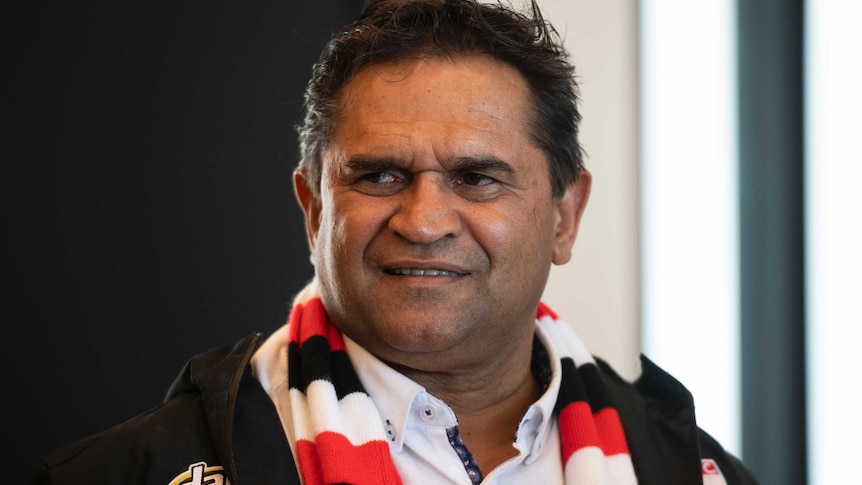 Nicky Winmar smiles wearing a red white and black striped scarf