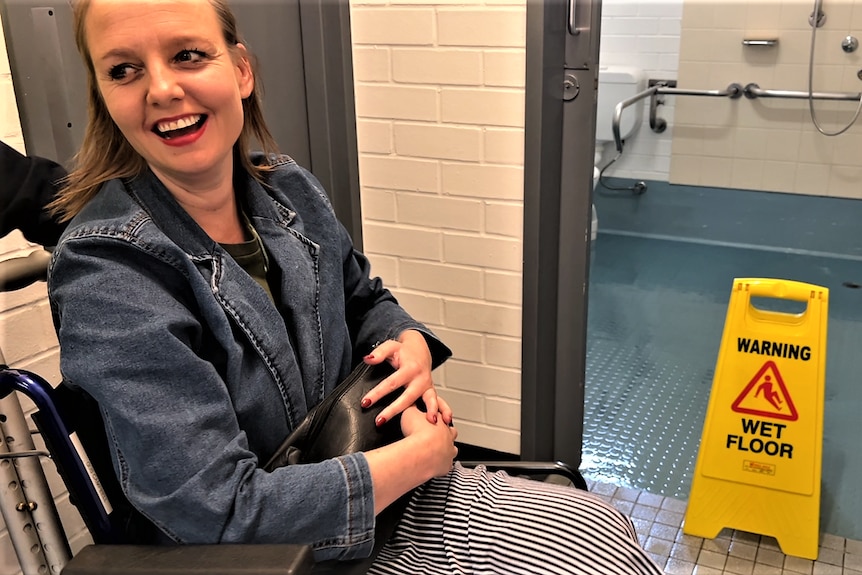 She sits in a wheelchair, the yellow 'wet floor' sign is behind her. Ausnew Home Care, NDIS registered provider, My Aged Care