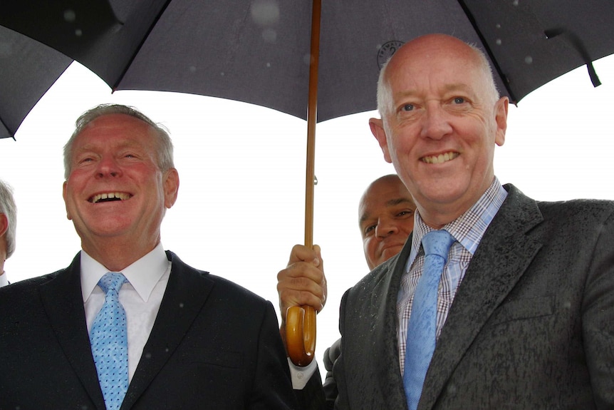 Colin Barnett shares an umbrella with Paul Miles as rain falls.