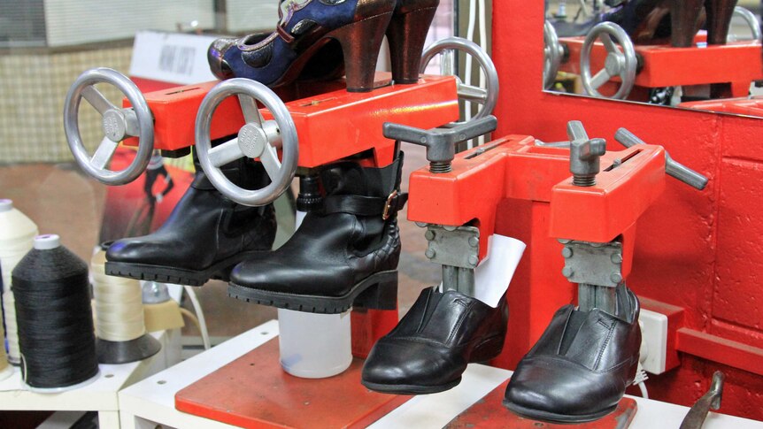 Black leather shoes with metal in them on a red machine being slowly stretched
