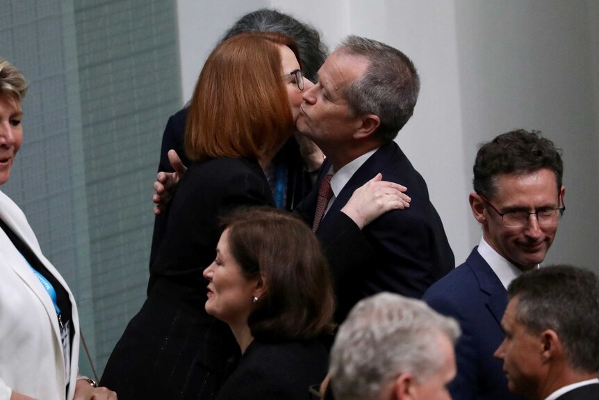 Julia Gillard and Bill Shorten embrace and kiss on the cheeks amid a crowd of MPs