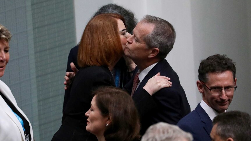 Julia Gillard and Bill Shorten embrace and kiss on the cheeks amid a crowd of MPs