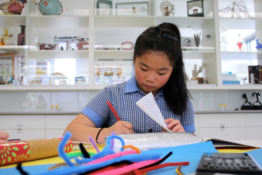 Angela Jia writes at a desk in school science lab.