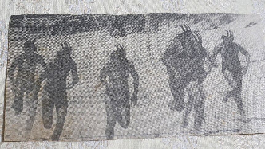 A newspaper clipping of teenage girls running on the sand, wearing striped caps showing which surf club they belong to.