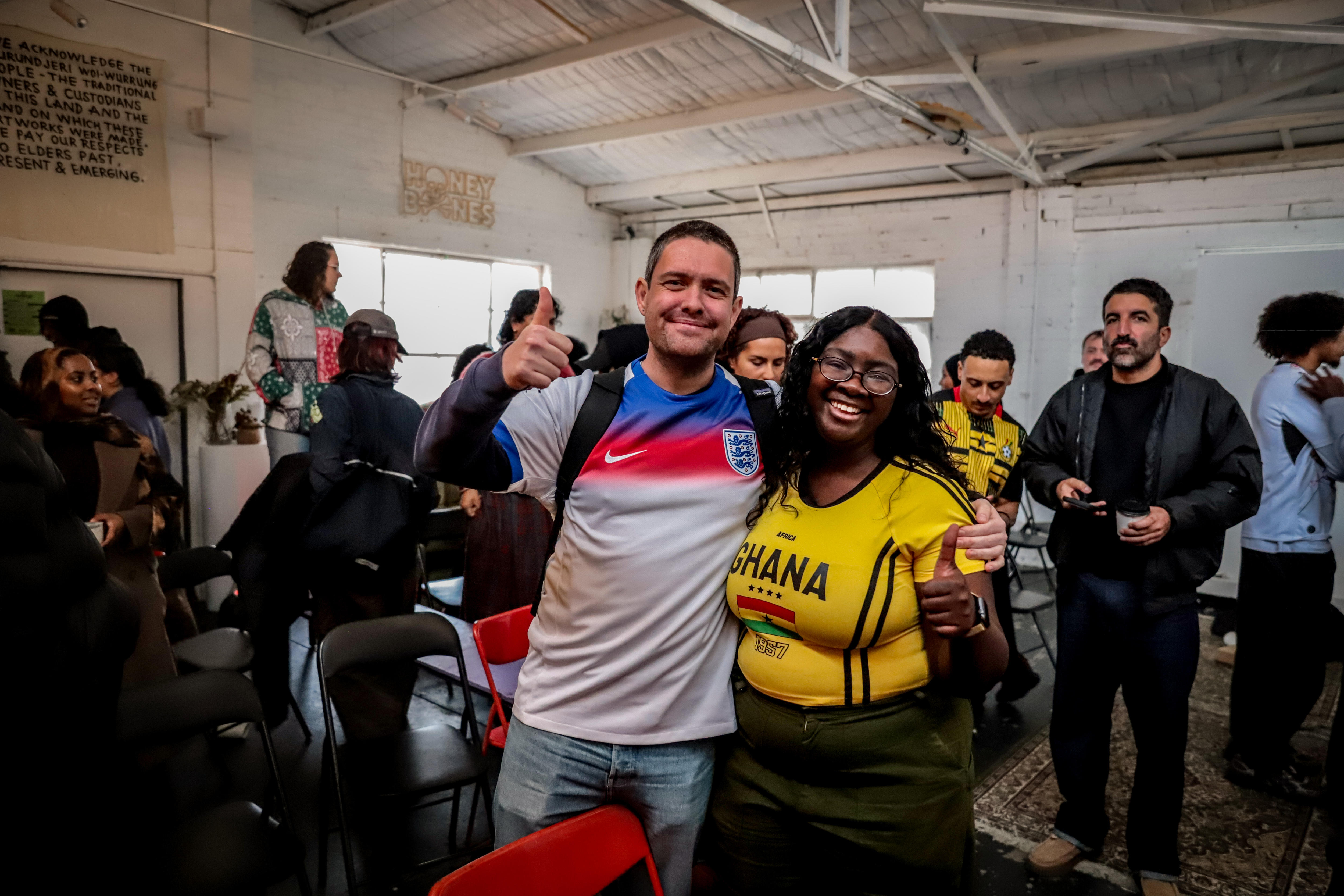 A man wearing a blue, white and red football jersey stands with his arm around a woman wearing a yellow jersey with GHANA on 