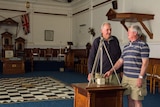 Masons Tony McKenzie and Wal Williams in the Masonic building at Forbes, NSW, with chequerboard tiles and ritual equipment.