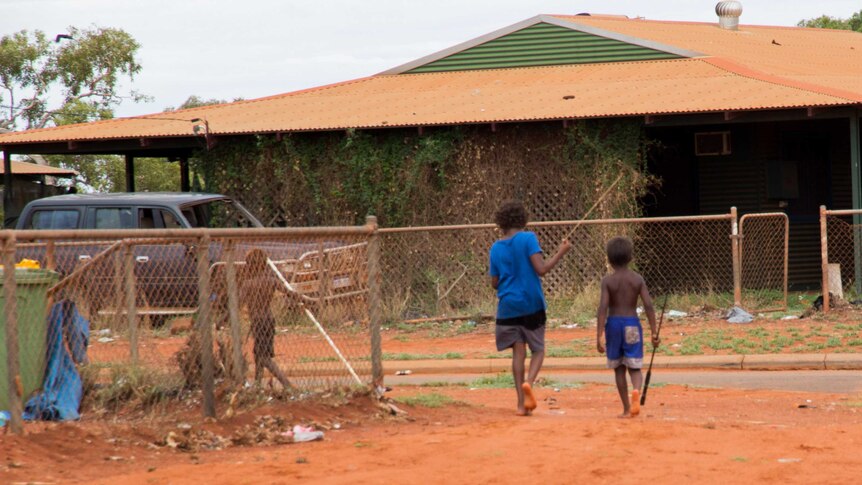 Two young indigenous boys walk barefoot, carrying spears.
