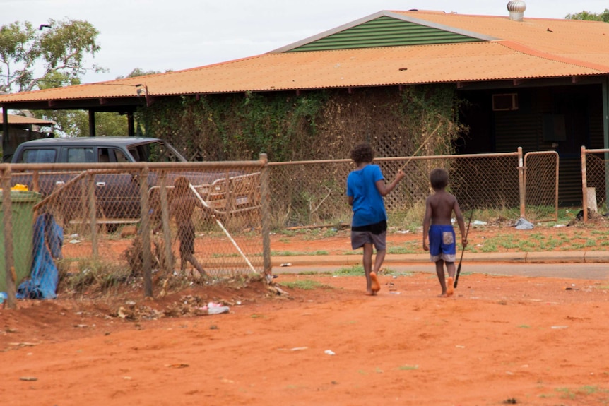 Two young indigenous boys walk barefoot, carrying spears.