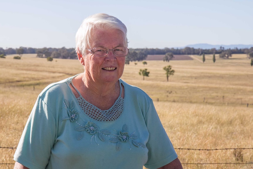 A woman in her 70s standing in front of a paddock