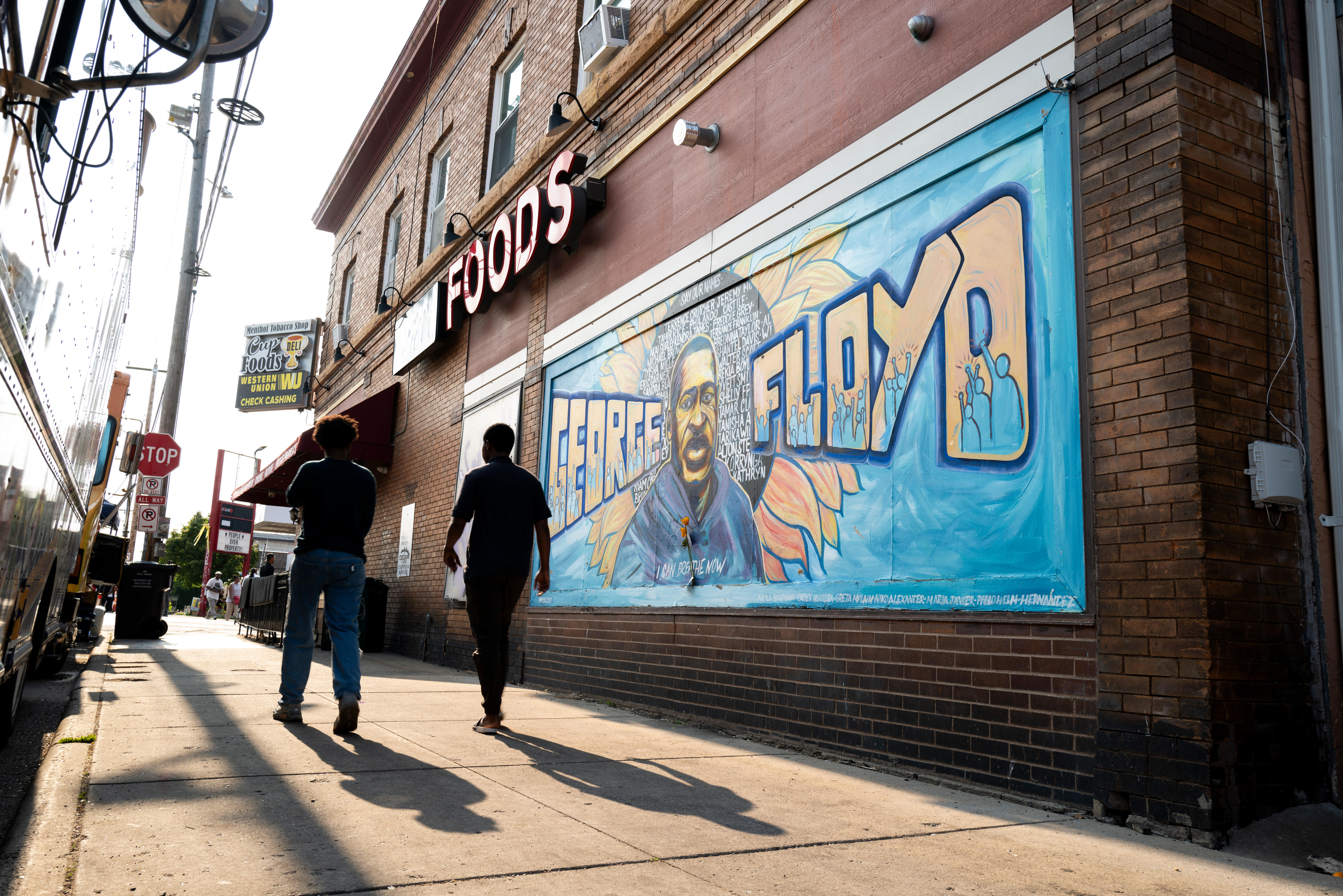 Two men walk past a portrait of George Floyd painted on a brick wall