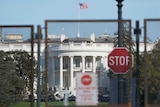 Security fencing surrounds the White House and a stop sign is pinned up in front of t